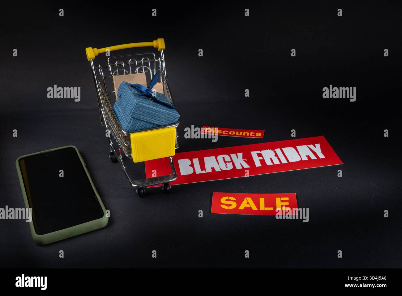 Miniatur-Einkaufswagen voller Geschenke steht auf schwarzem freitagsschild neben Smartphone auf schwarzem Hintergrund, Online-Shopping-Konzept Stockfoto