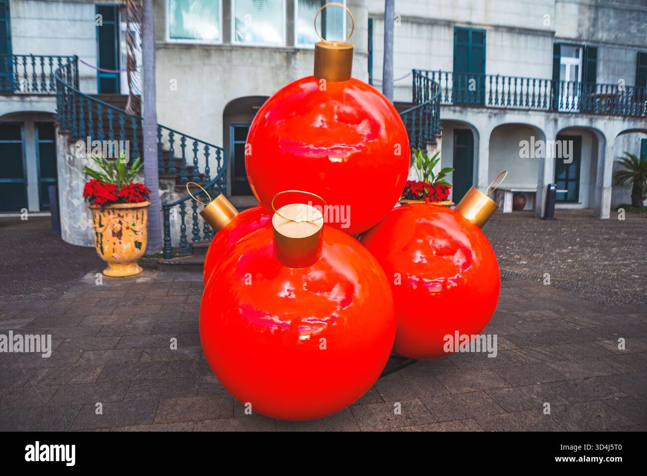 Übergroße rote Weihnachtsschmuck mit goldenen Kappen sitzen auf dem gepflasterten plaza und reflektieren das Licht. Farbenfrohe rote Weihnachtsdekoration im Kontrast zu stumm Stockfoto
