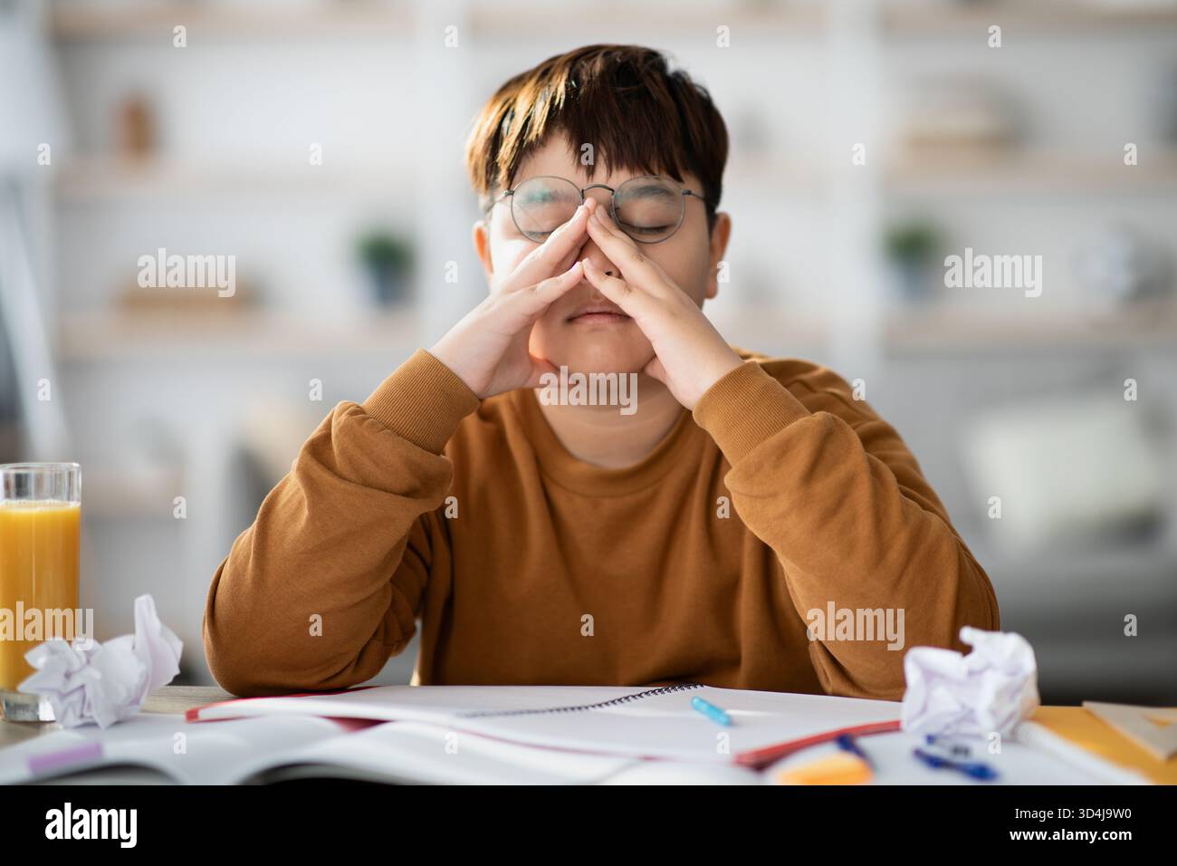 Müder japanischer Junge, der zu Hause am Schulprojekt arbeitet, auf der Suche nach kreativen Ideen Stockfoto