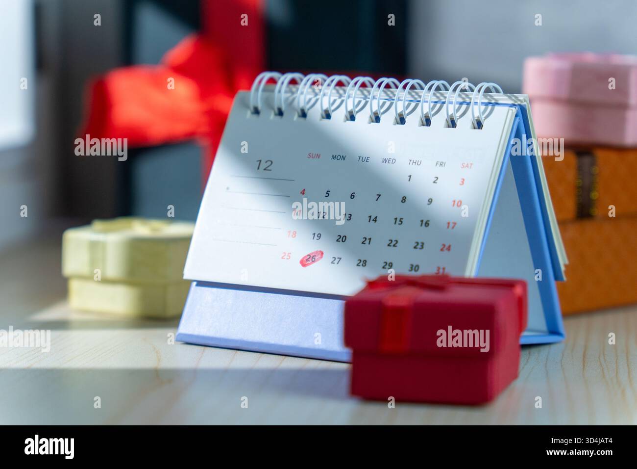 Ein Dezember-Schreibtischkalender, der Weihnachten und den zweiten Weihnachtsfeiertag hervorhebt, ist umgeben von farbenfrohen Geschenkboxen in verschiedenen Größen, die Weihnachtsverkäufe symbolisieren Stockfoto