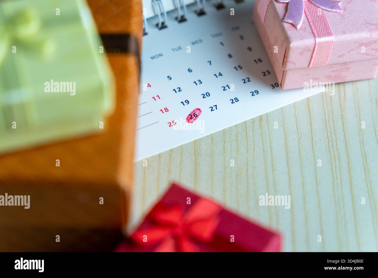 Nahaufnahme eines Kalenders mit dem 26. Datum in rot eingekreist, umgeben von bunten Geschenkboxen. Weihnachtsfeier und Verkaufskonzept nach Feiertag. Stockfoto