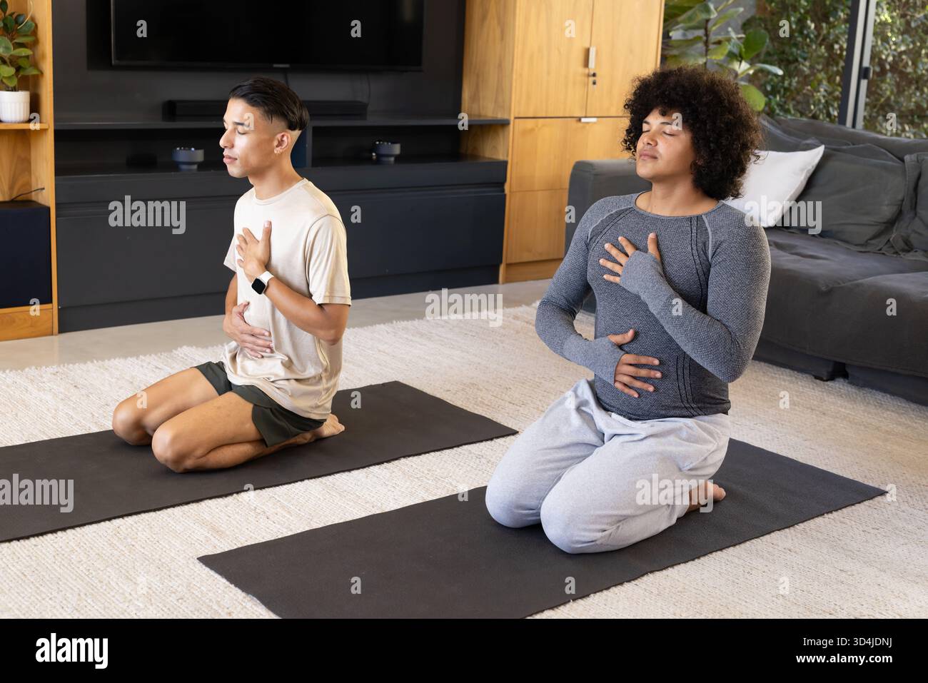 Übungen zum Atmen verschiedene männliche Freunde kniend auf Yogamatten im Wohnzimmer, mit Fernseher Stockfoto