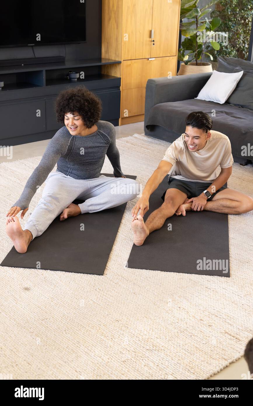 Verschiedene männliche Freunde strecken, die Zehen auf schwarzen Yogamatten im Wohnzimmer erreichen, mit Topfpflanzen Stockfoto