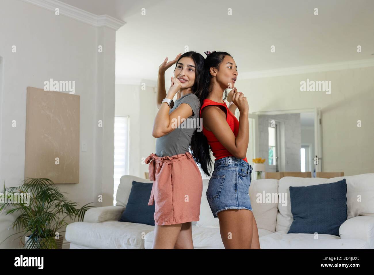 Verschiedene weibliche Freunde stehen im Wohnzimmer, mit Sofa, Pflanzen- und Leinwandkunst Stockfoto