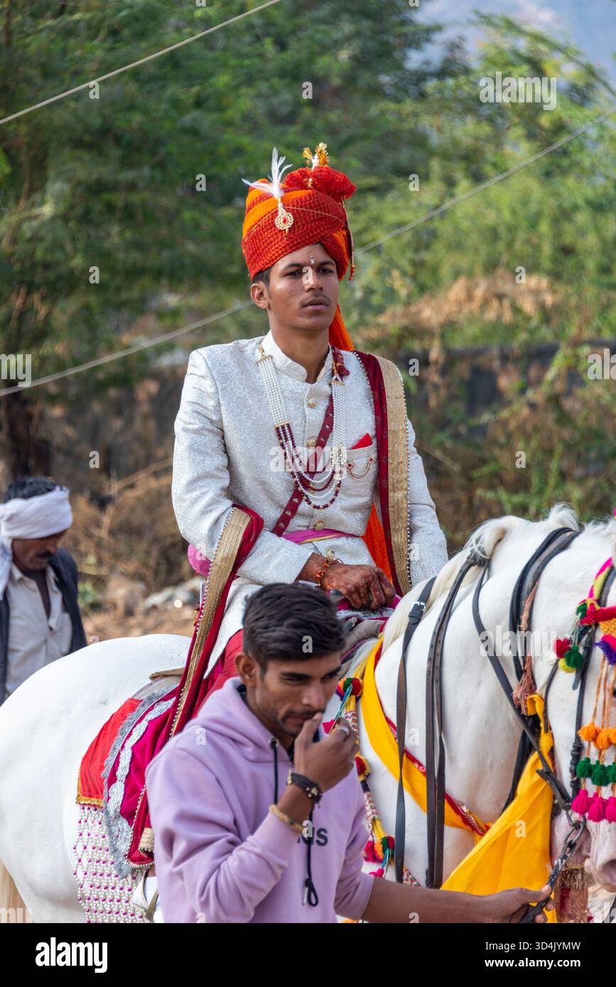Indischer Bräutigam in traditioneller Hochzeitskleidung auf einem dekorierten Pferd während Baraat. Pushkar, Indien, 28. Januar 2024 Stockfoto