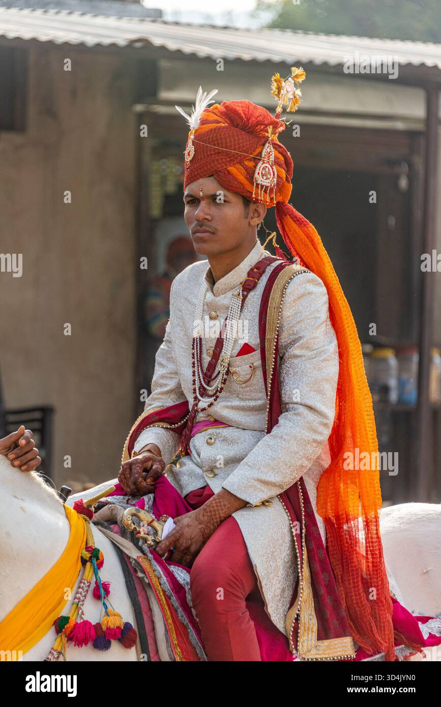 Indischer Bräutigam in traditioneller Hochzeitskleidung auf einem dekorierten Pferd während Baraat. Pushkar, Indien, 28. Januar 2024 Stockfoto