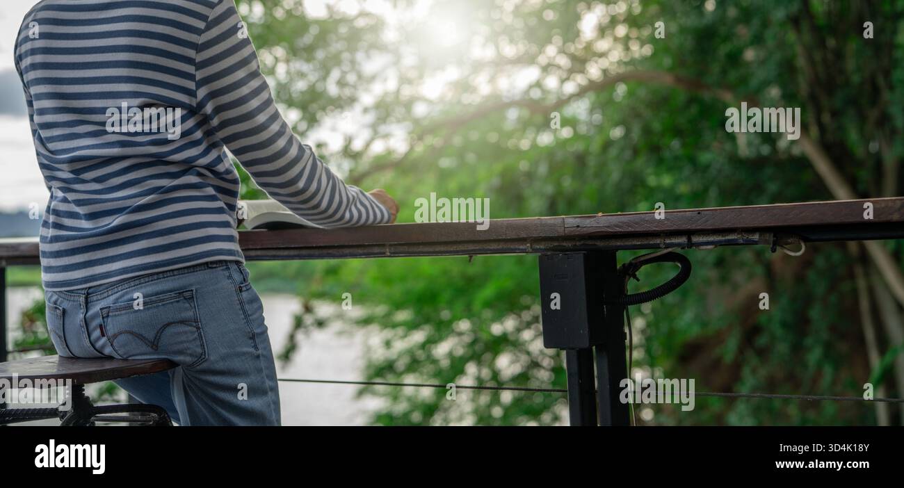 Rückansicht einer Frau, die ein Buch liest, in einem umweltfreundlichen Hotel im Freien mit Grünflächen. Selfcare Digital Detox Konzept Retreat psychische Gesundheit Wellness Natur Stockfoto