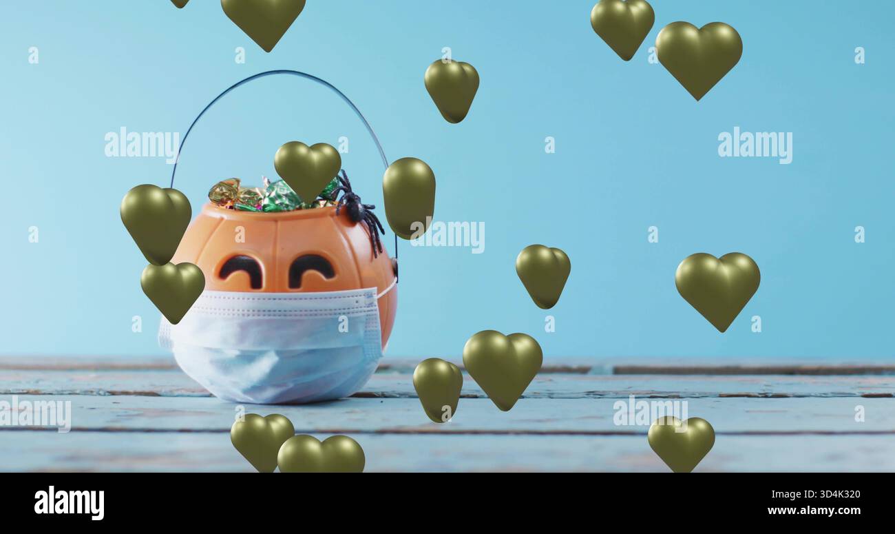 Mit orangefarbenem Kürbiseimer mit blauer Maske auf bemaltem Tisch, mit Süßigkeiten, Spinne, goldenen Herzen Stockfoto
