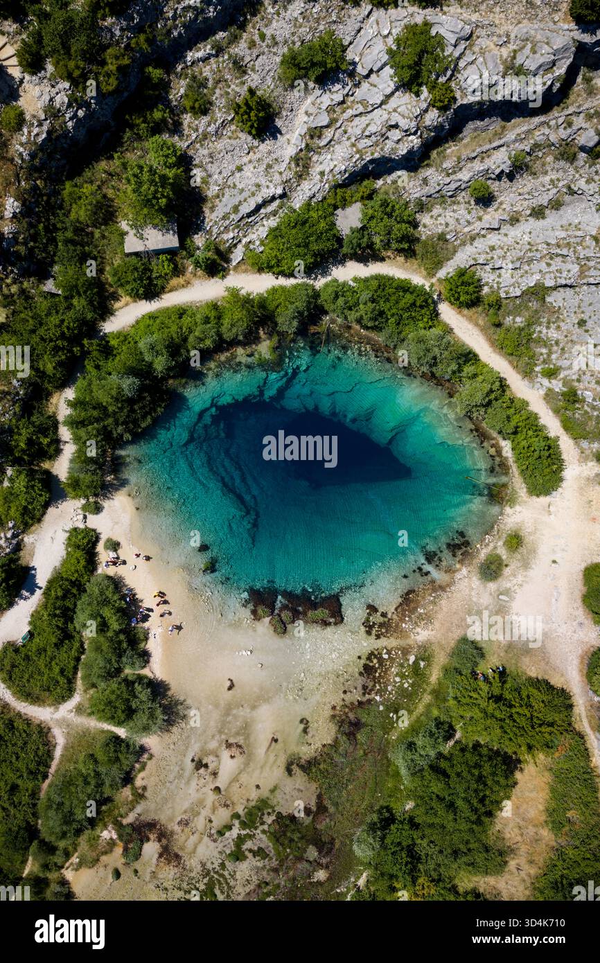 Der Blick aus der Luft auf ein faszinierendes tiefblaues Auge der Quelle des Cetina River steht in dramatischem Kontrast zur umliegenden felsigen Landschaft, Cetina, Kroatien. Stockfoto