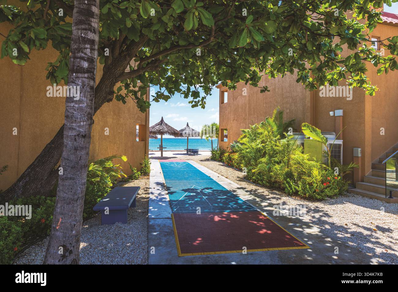 Wunderschöner Blick auf den tropischen Hotelgang mit Spielplatz im Hintergrund des Karibischen Meeres und Palmen. Aruba. Stockfoto