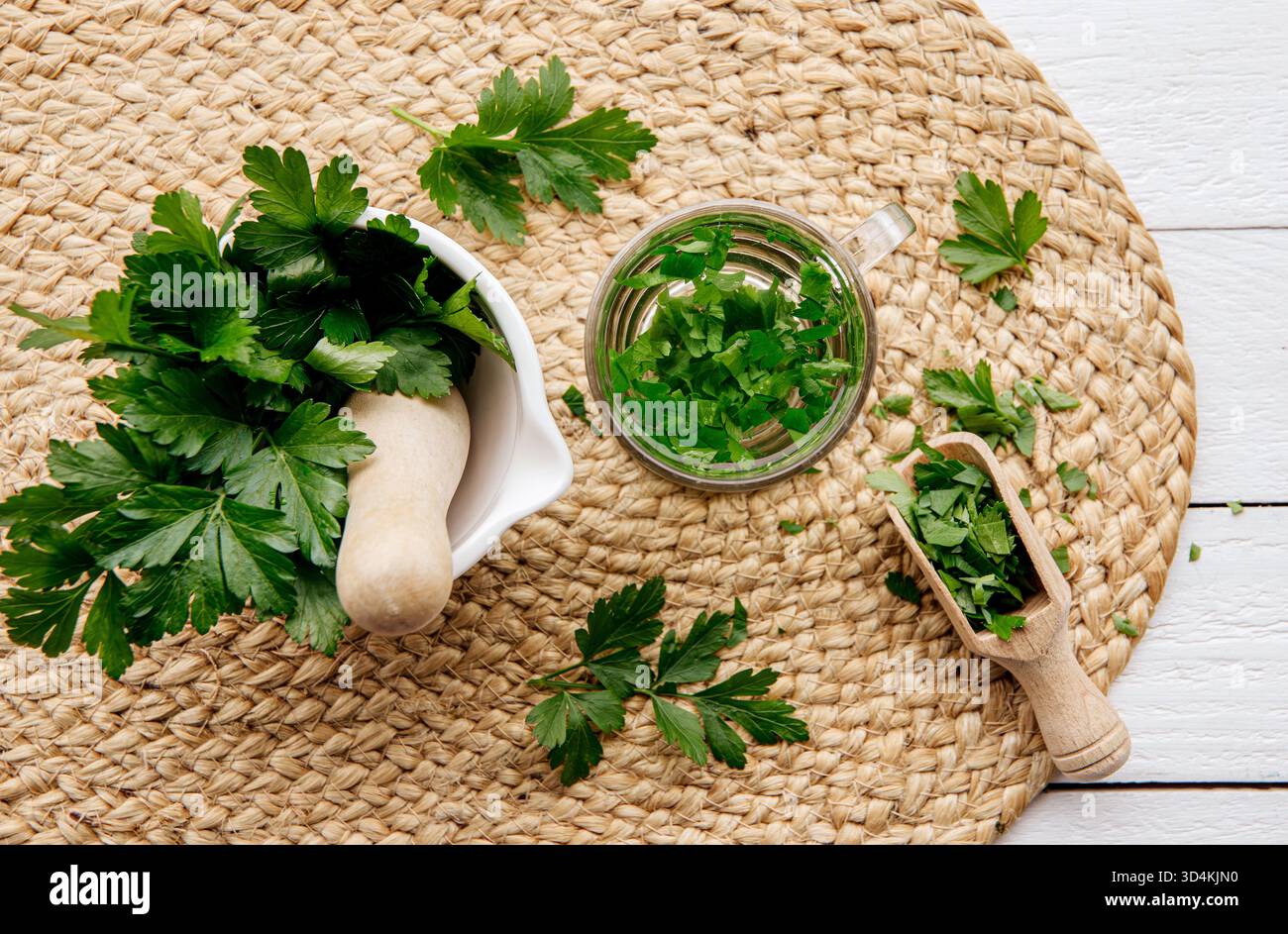 Ober-Ansicht von hausgemachtem Kräuter-Heiltee aus Petersilie Petroselinum crispum. Grüne Blätter in der Teetasse auf weißem Holzhintergrund. Stockfoto
