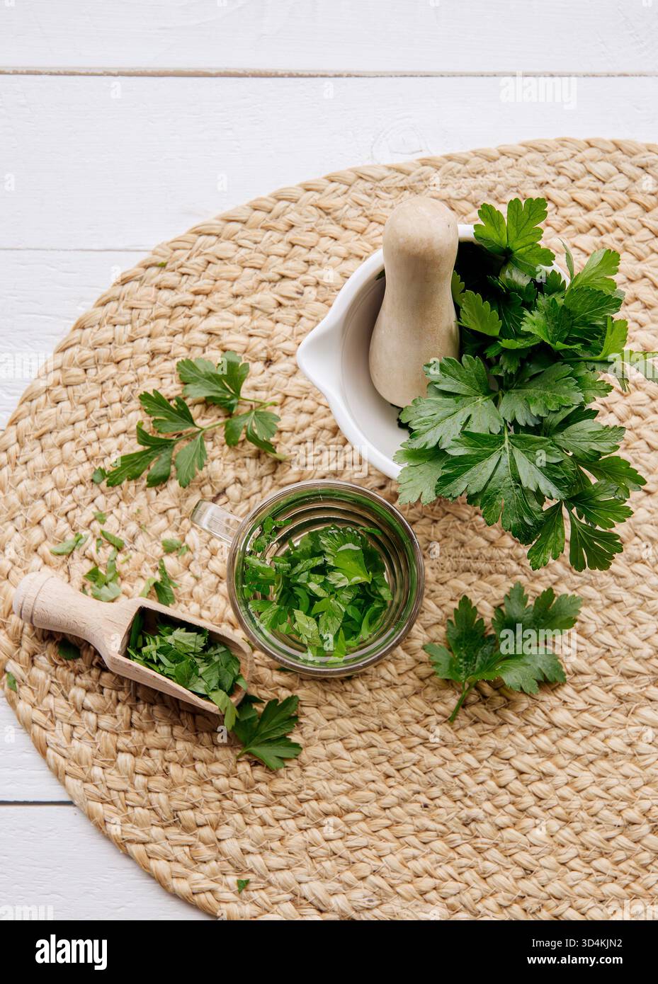 Ober-Ansicht von hausgemachtem Kräuter-Heiltee aus Petersilie Petroselinum crispum. Grüne Blätter in der Teetasse auf weißem Holzhintergrund. Stockfoto