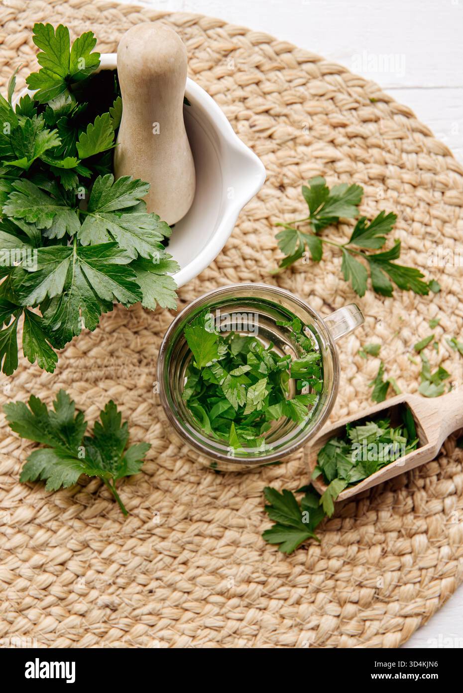 Ober-Ansicht von hausgemachtem Kräuter-Heiltee aus Petersilie Petroselinum crispum. Grüne Blätter in der Teetasse auf weißem Holzhintergrund. Stockfoto