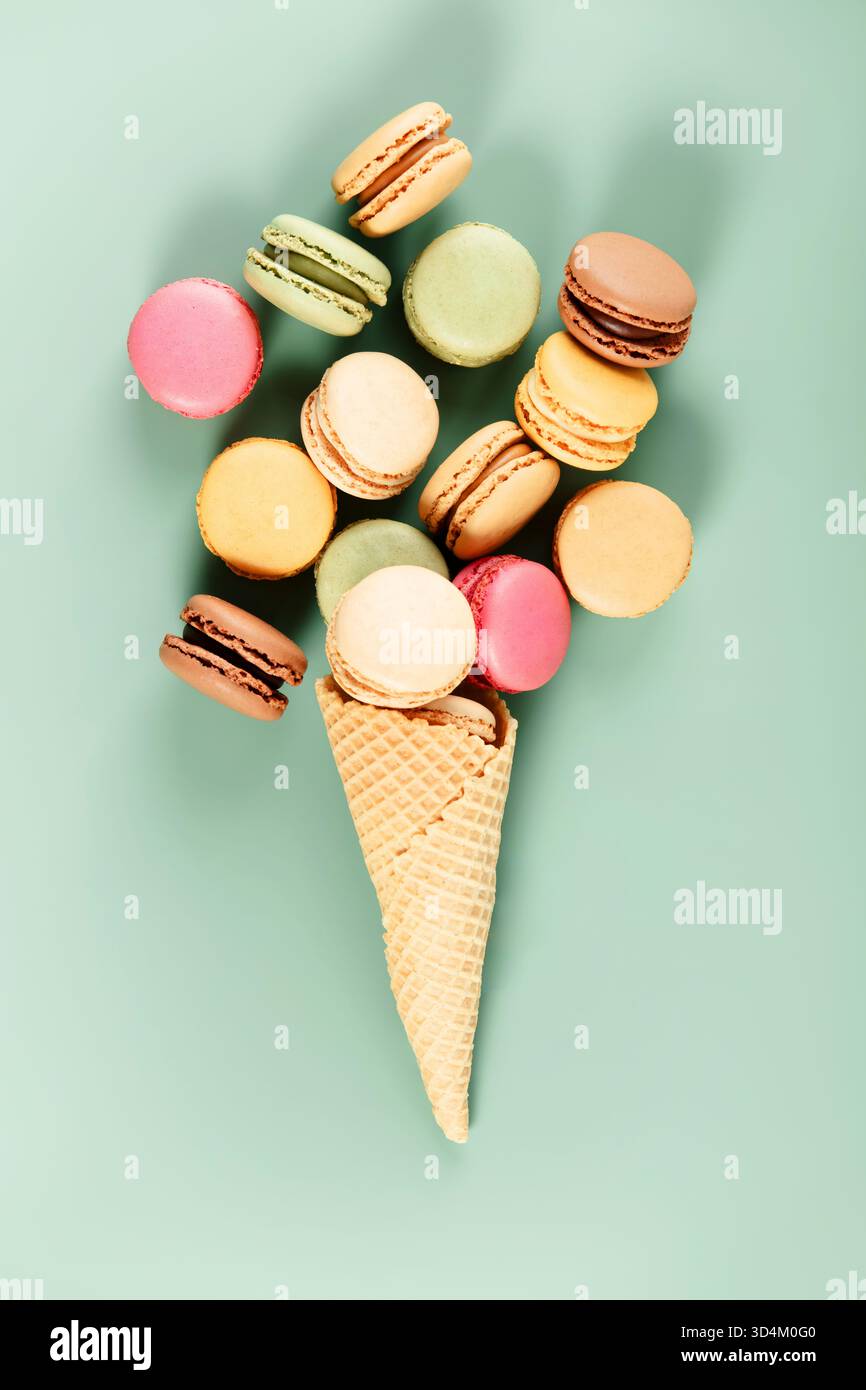 Kreative flache Lage aus verschiedenen Macarons, die in einer Waffelkugel wie Eis angeordnet sind, auf einem weichen mintgrünen Hintergrund. Stockfoto