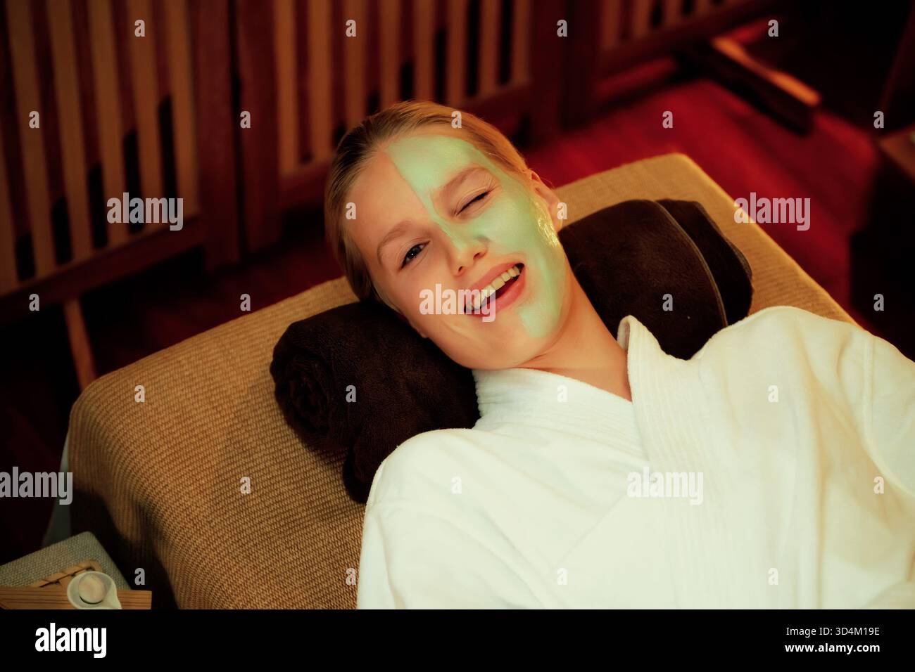 Die ruhige Atmosphäre des Spa-Salons, die lächelnde und verjüngende Kundin mit einer luxuriösen Gesichtscreme-Massage mit warmer Kerze. Gesichtshaut Stockfoto