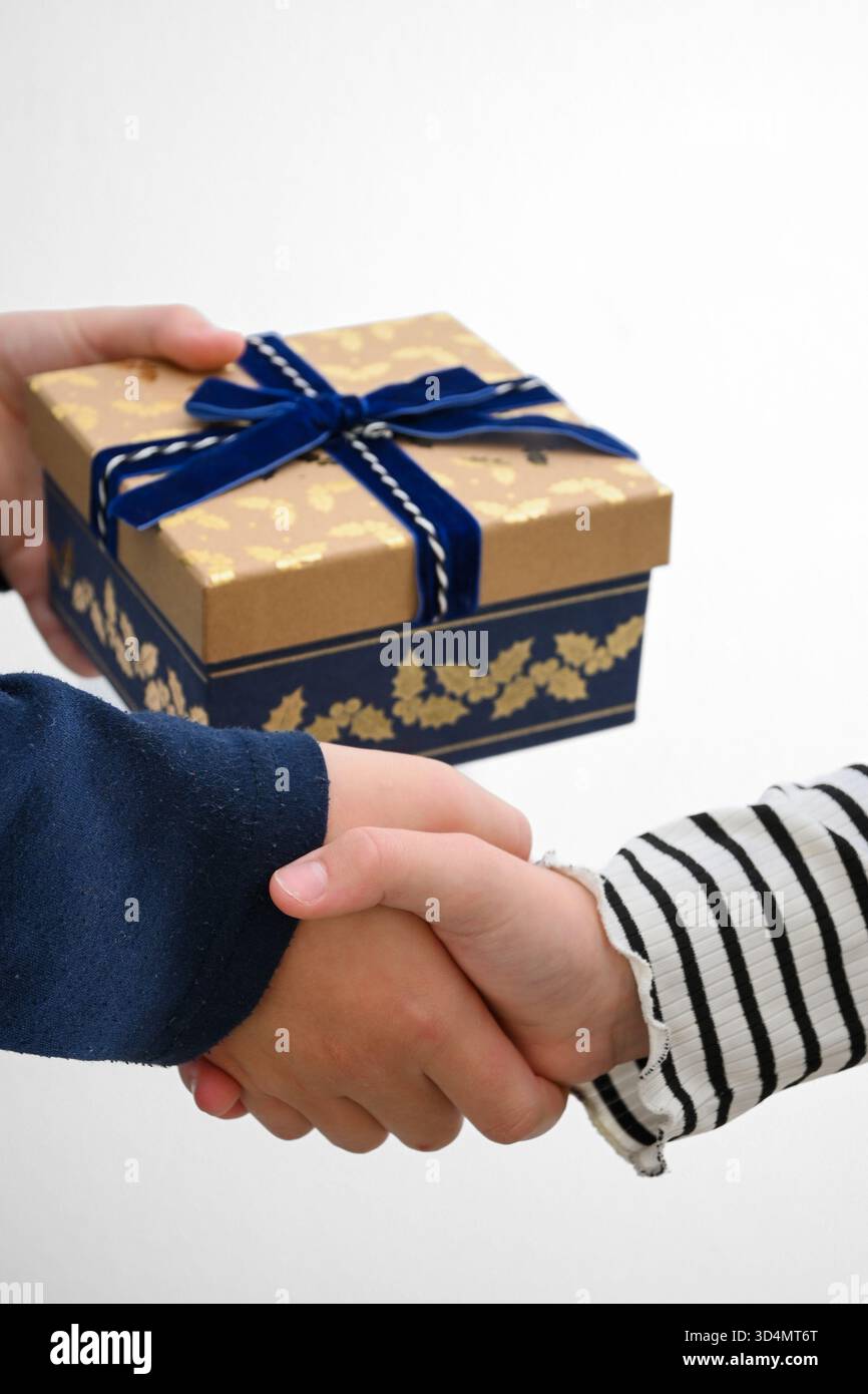 Hände tauschen ein wunderschön gewickeltes Geschenk aus und schütteln die Hände, was eine erfolgreiche Transaktion symbolisiert. Stockfoto