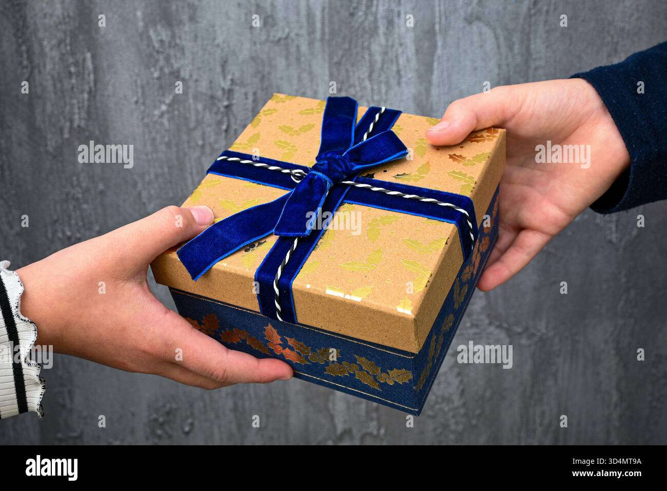 Zwei Hände tauschen eine verzierte braune und blaue Geschenkbox aus. Stockfoto