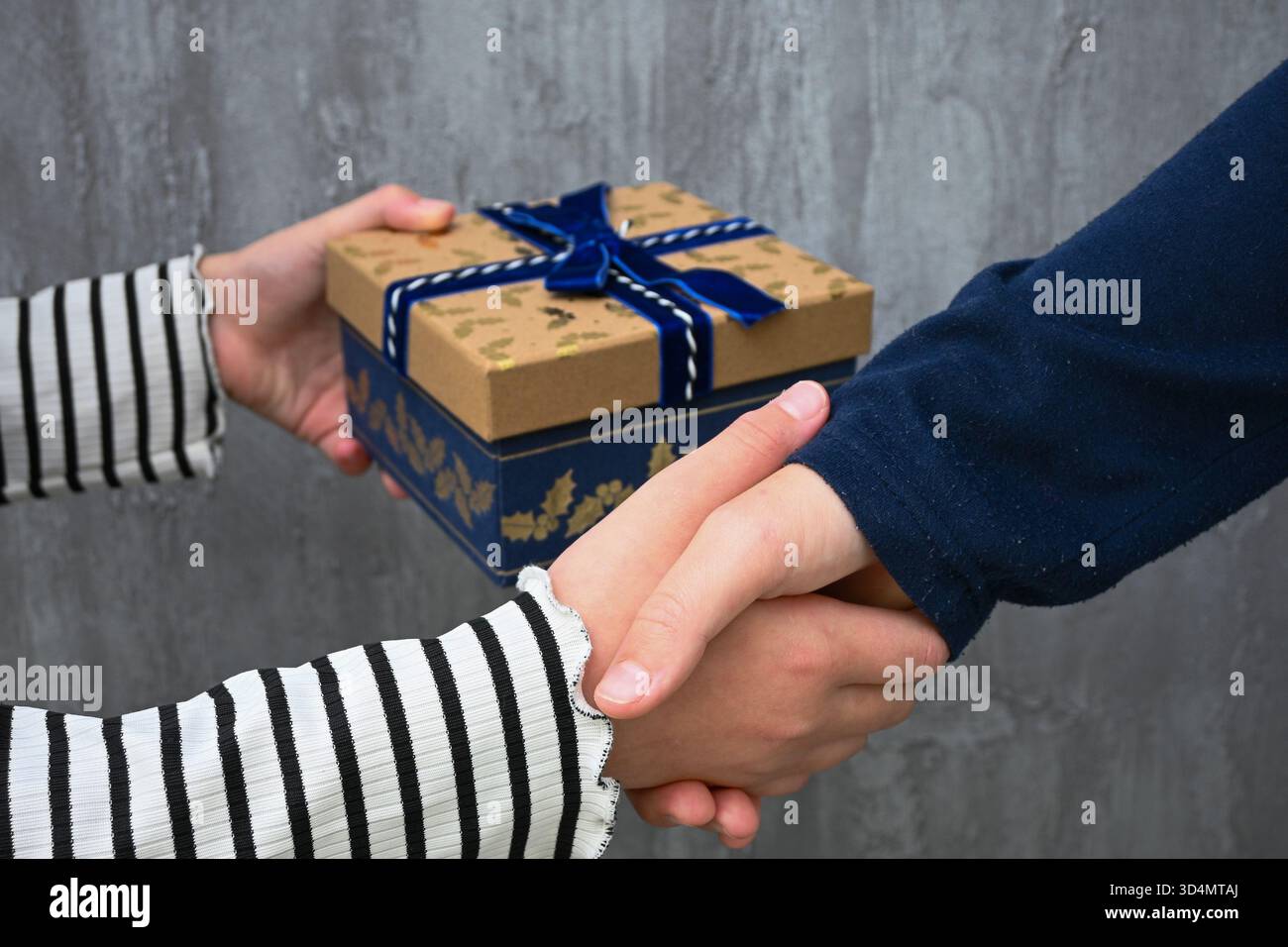 Hände tauschen eine wunderschön verpackte Geschenkbox aus, während Sie die Hände schütteln, was das Geben und die Zustimmung symbolisiert. Stockfoto