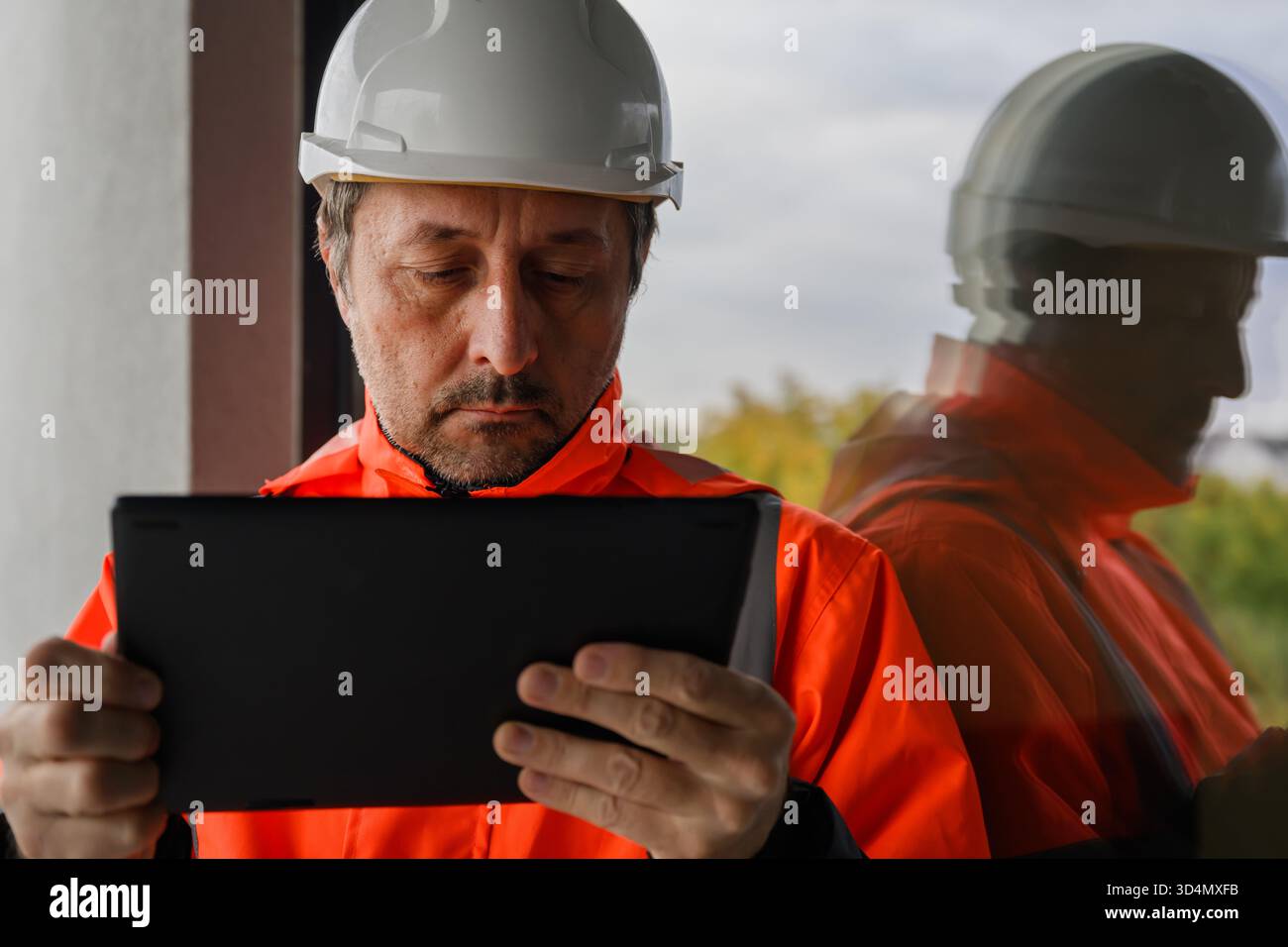 Bauingenieur in Sicherheitsjacke und Schutzhelm mit digitalem Tablet auf der Baustelle, Symbol für Technologie, Steuerung und modernes Projektmanagement. S Stockfoto