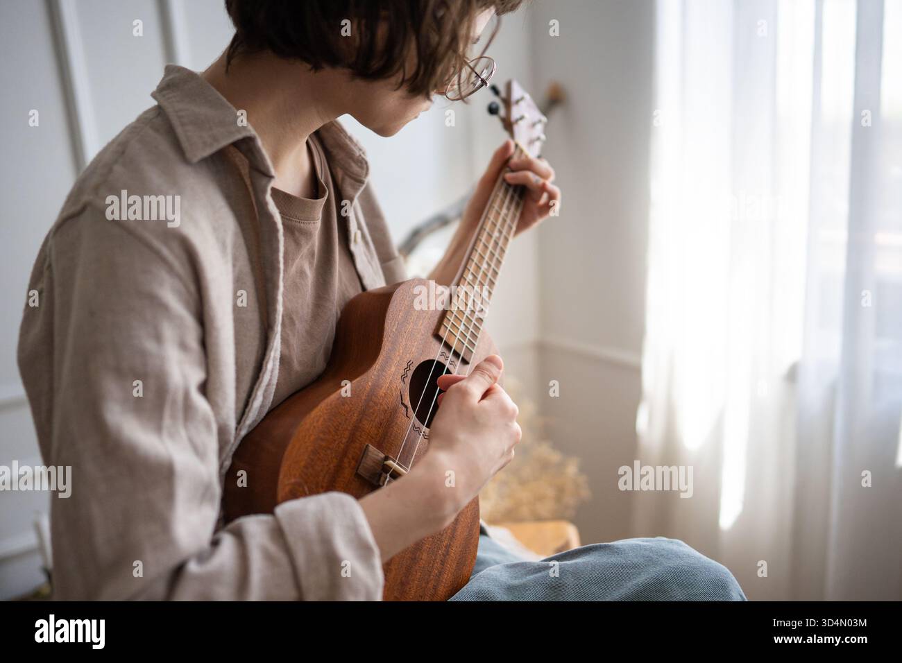 Junge Frau, die zu Hause Ukulelakkorde einstudiert, Fingerplatzierung und Schlagtechnik verfeinert Stockfoto