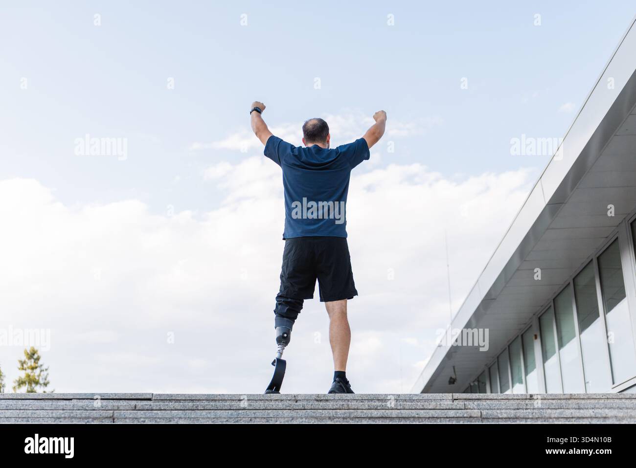 Mann mit einer Prothese, die die Arme zum Sieg hebt, nachdem er erfolgreich gelaufen ist, lange Straßentreppen hinauf. Behinderung, Leistung und Motivation Stockfoto