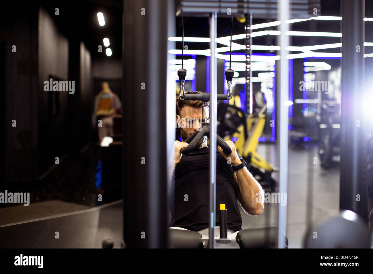 In einem eleganten Fitnessstudio, umgeben von fortschrittlichen Geräten und lebendiger Beleuchtung, wird ein Mann Krafttraining absolvieren. Stockfoto