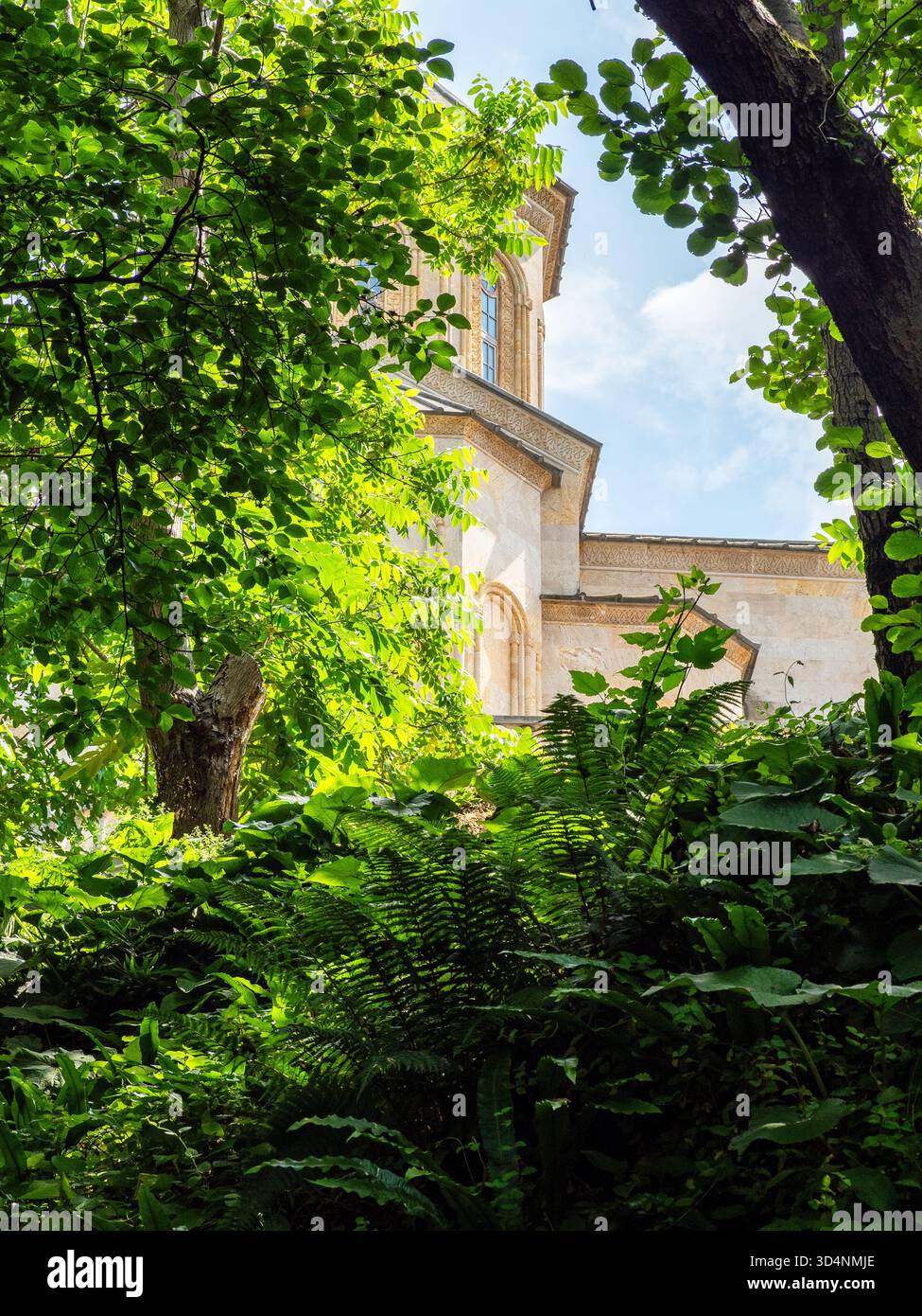Blick auf das Gebäude der Heiligen Dreifaltigkeitskirche im Kloster Tsminda Sameba durch üppiges grünes Laub in Batumi City am sonnigen Sommertag, Georgia Stockfoto