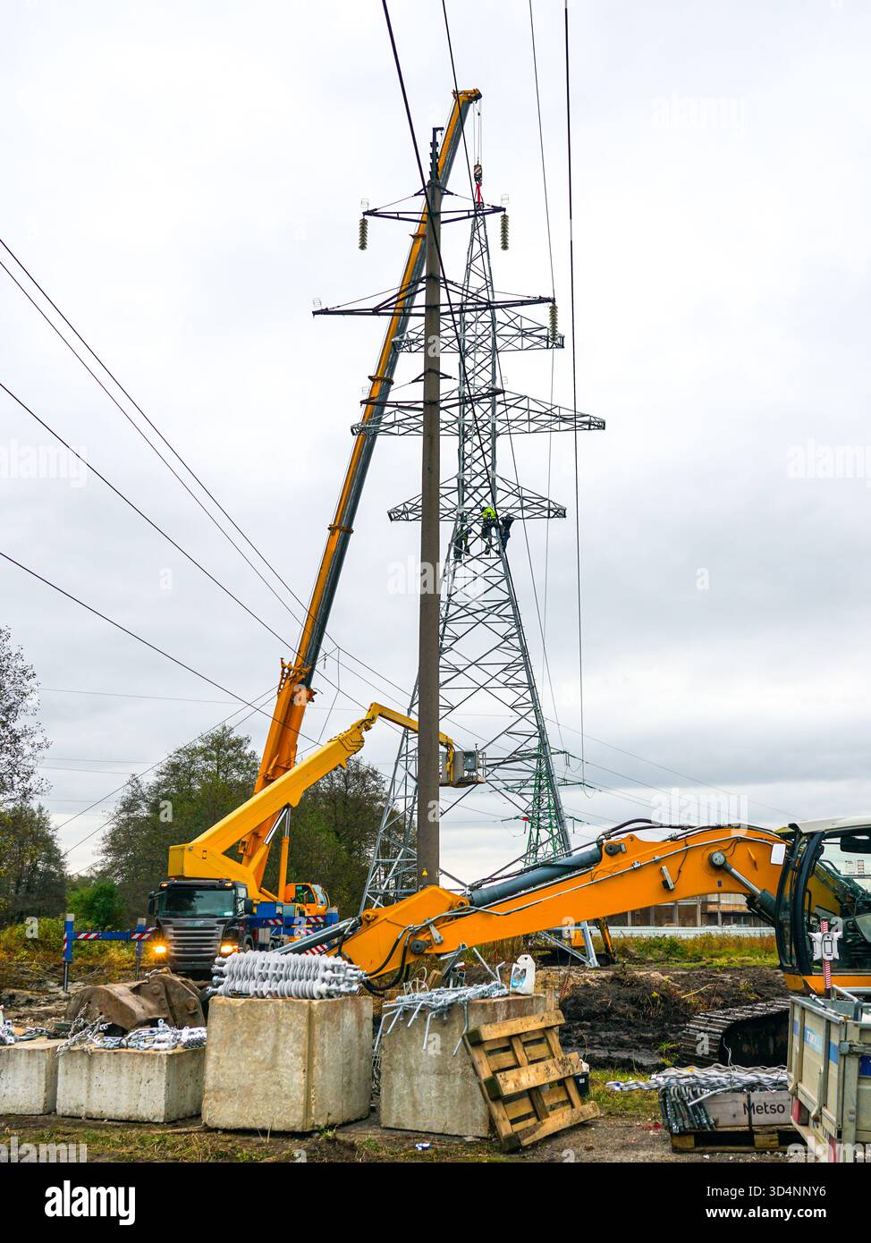 Arbeiter und Kräne installieren Hochspannungs-Übertragungsturm auf der Baustelle und zeigen Teamarbeit, technische Präzision und moderne Energieinfrastruktur Stockfoto