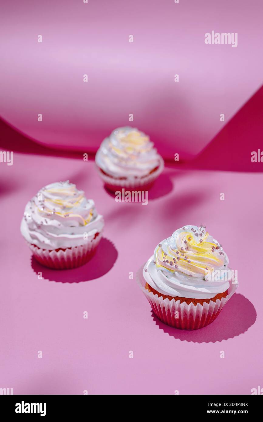 Essen, drei dekorierte Cupcakes mit cremiger Zuckerguss vor leuchtendem rosa Hintergrund Stockfoto