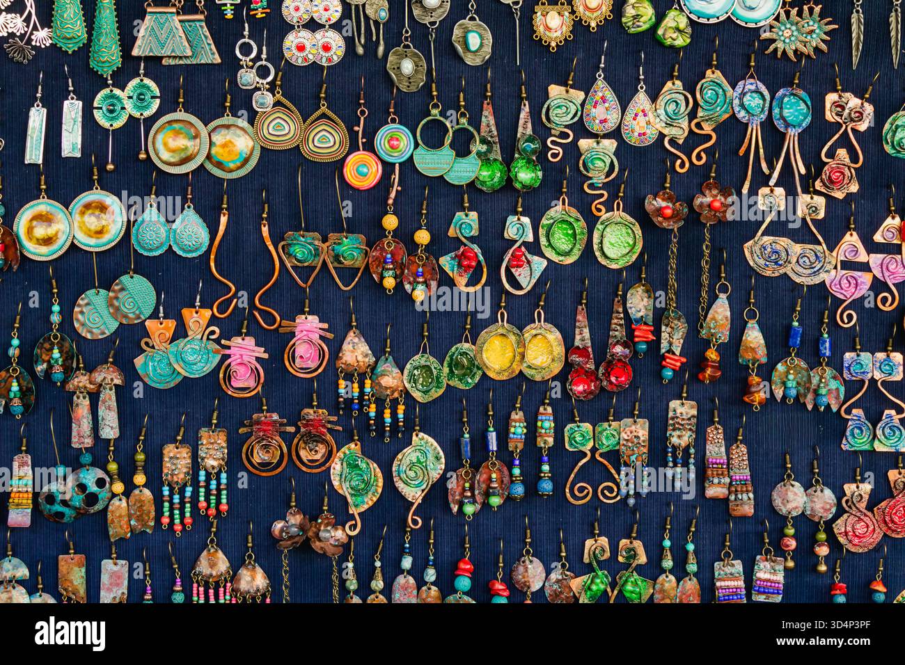 Eine lebendige Kollektion handgefertigter Ohrringe in verschiedenen Designs und Materialien wird auf einem dunklen Stoffhintergrund präsentiert. Das Arrangement zeigt die cre Stockfoto