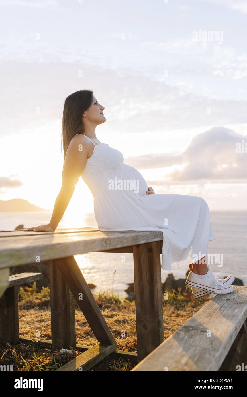 Porträt einer schwangeren Frau gegen eine ozeanische Landschaft bei Sonnenuntergang in Galicien, Spanien Stockfoto