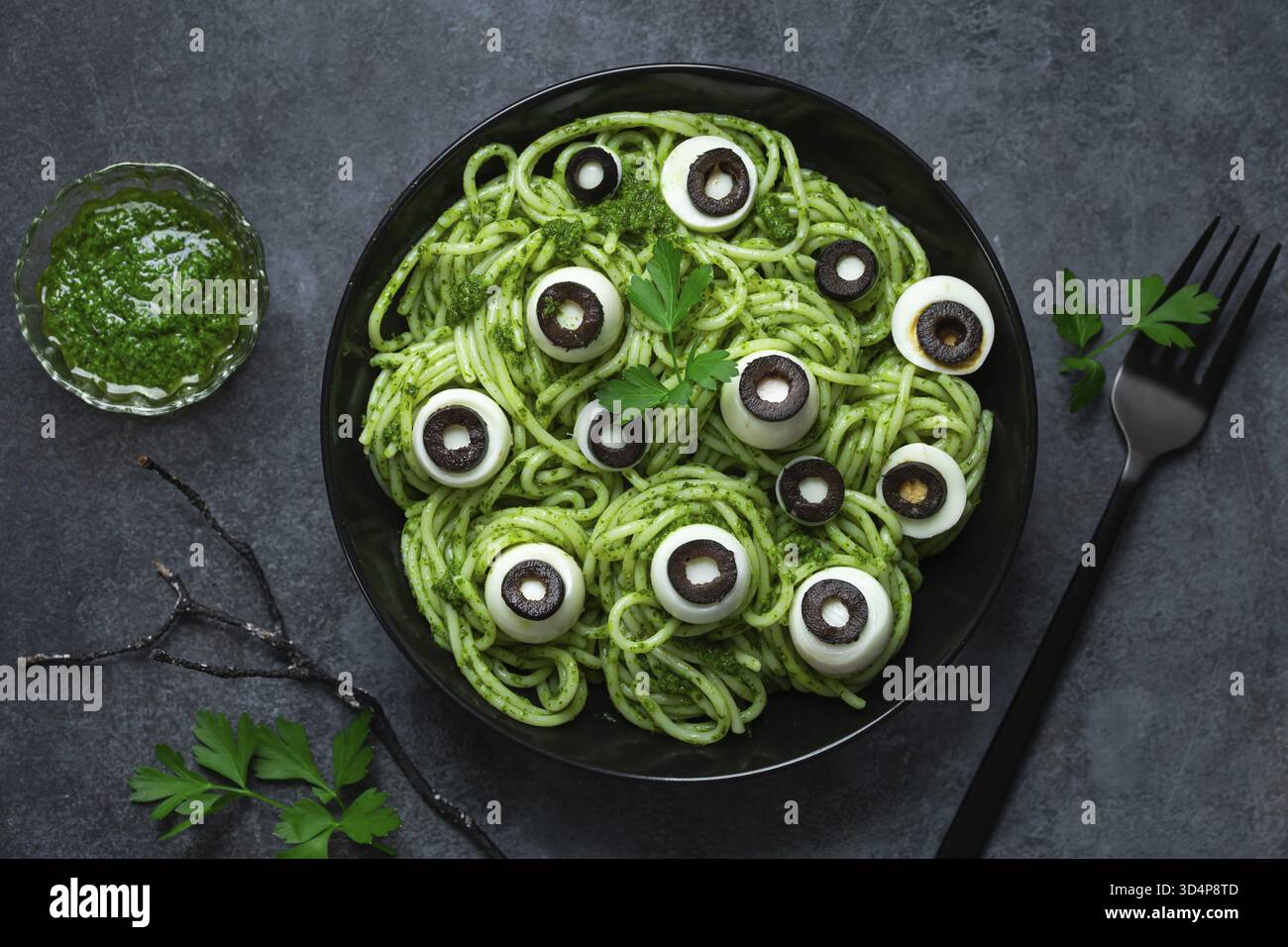 Essen, Spaghetti-Pasta mit grüner Pesto-Sauce, wachteleigen und Augen aus schwarzen Oliven, leckere und lustige Idee für Halloween-Abendessen Stockfoto