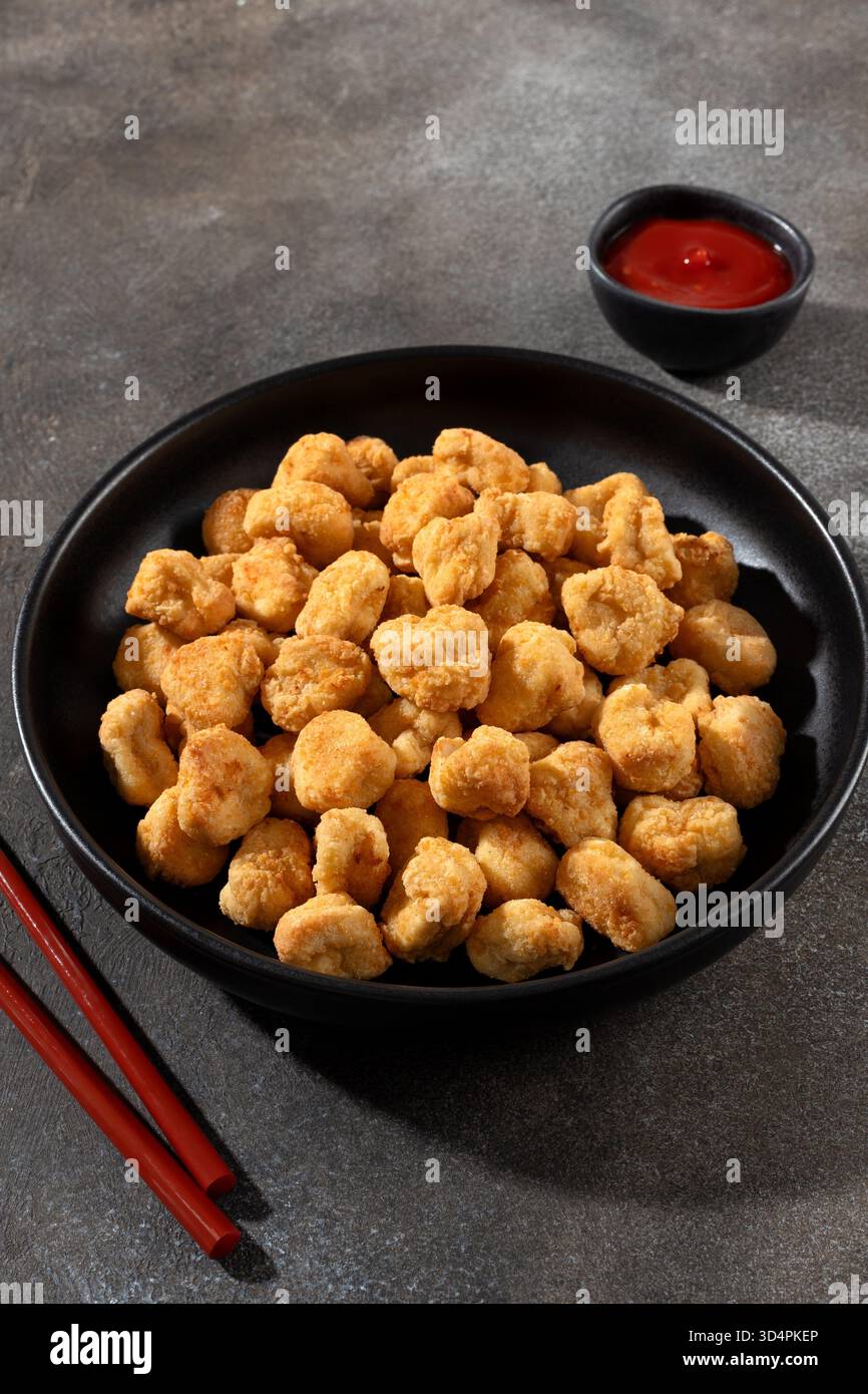 Goldenes knuspriges Hühnerpopcorn mit Ketchup auf grauem Hintergrund. Fastfood- und Snackkonzept. Stockfoto