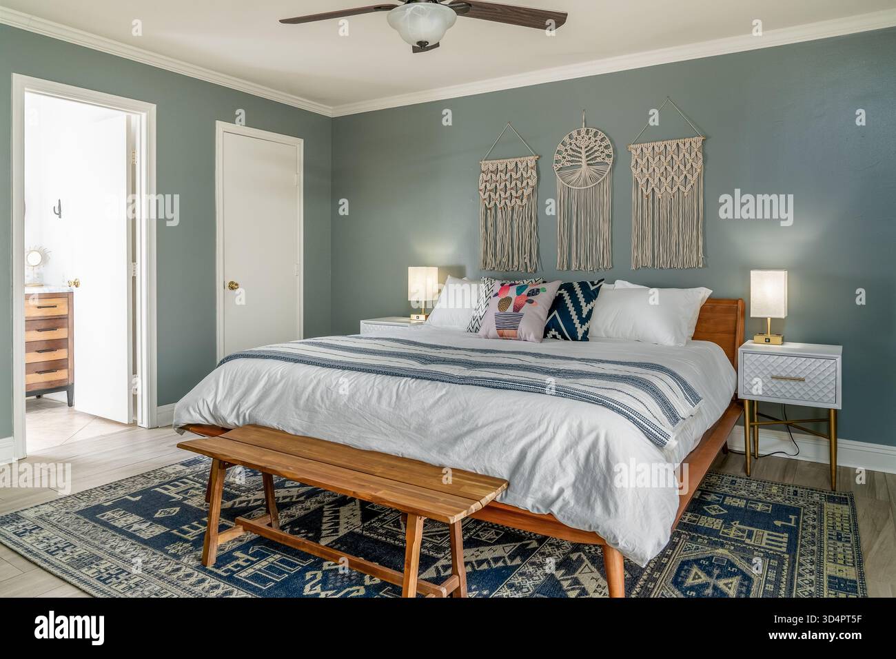 Modernes Boho-Schlafzimmer. Bett, Kissen, blaue Wand, Makramee-Hänge, Lampen, Nachttische. Holzbank und Teppich. Stockfoto