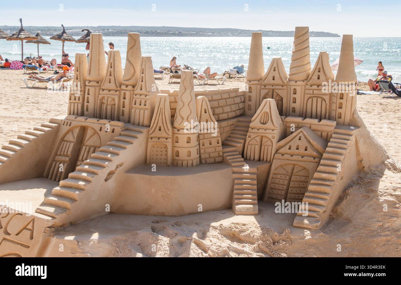 Große und komplizierte Sandburg-Skulptur mit Türmen und Treppen an einem überfüllten Strand in der Nähe des Meeres Stockfoto