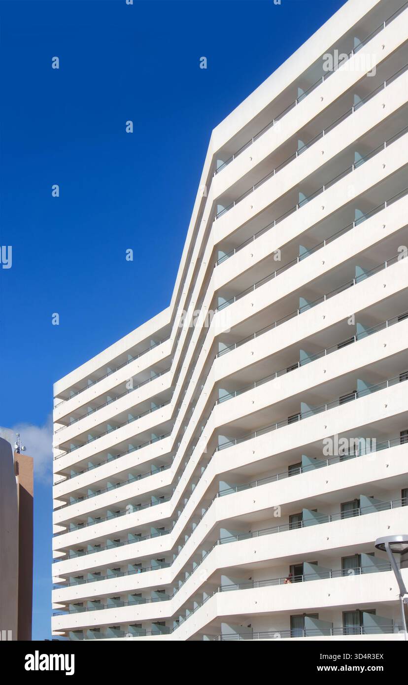 Modernes weißes Wohngebäude mit markanten eckigen Balkonen unter klarem tiefblauem Himmel Stockfoto