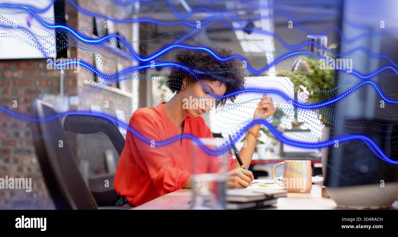 Schreibende Frau in roter Bluse, die sich mit glasblauen Überzügen am modernen Schreibtisch nach vorne lehnt Stockfoto
