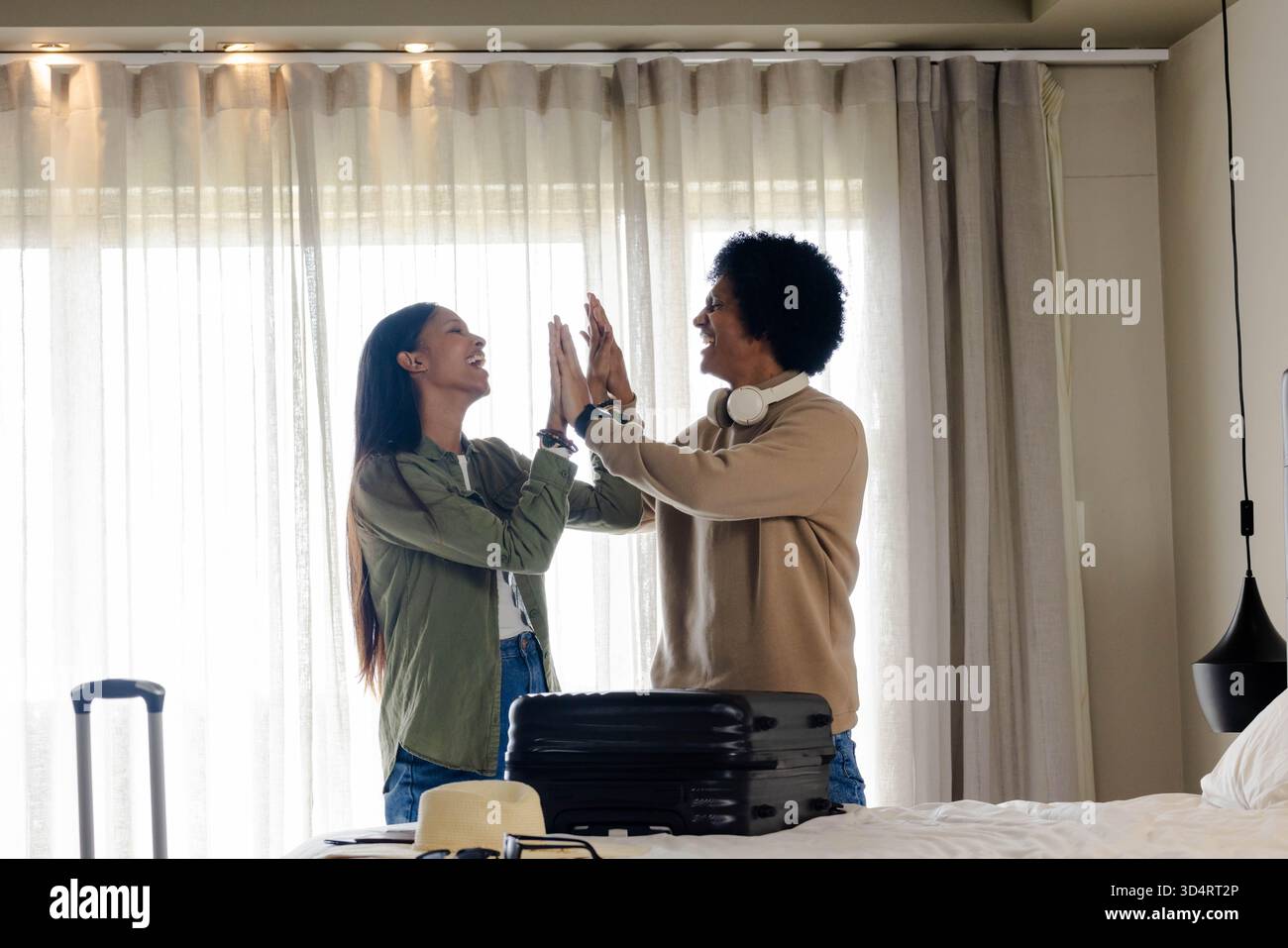 Ein vielseitiges Paar mit schwarzem Koffer, Strohhut und Sonnenbrille steht im Hotelzimmer Stockfoto