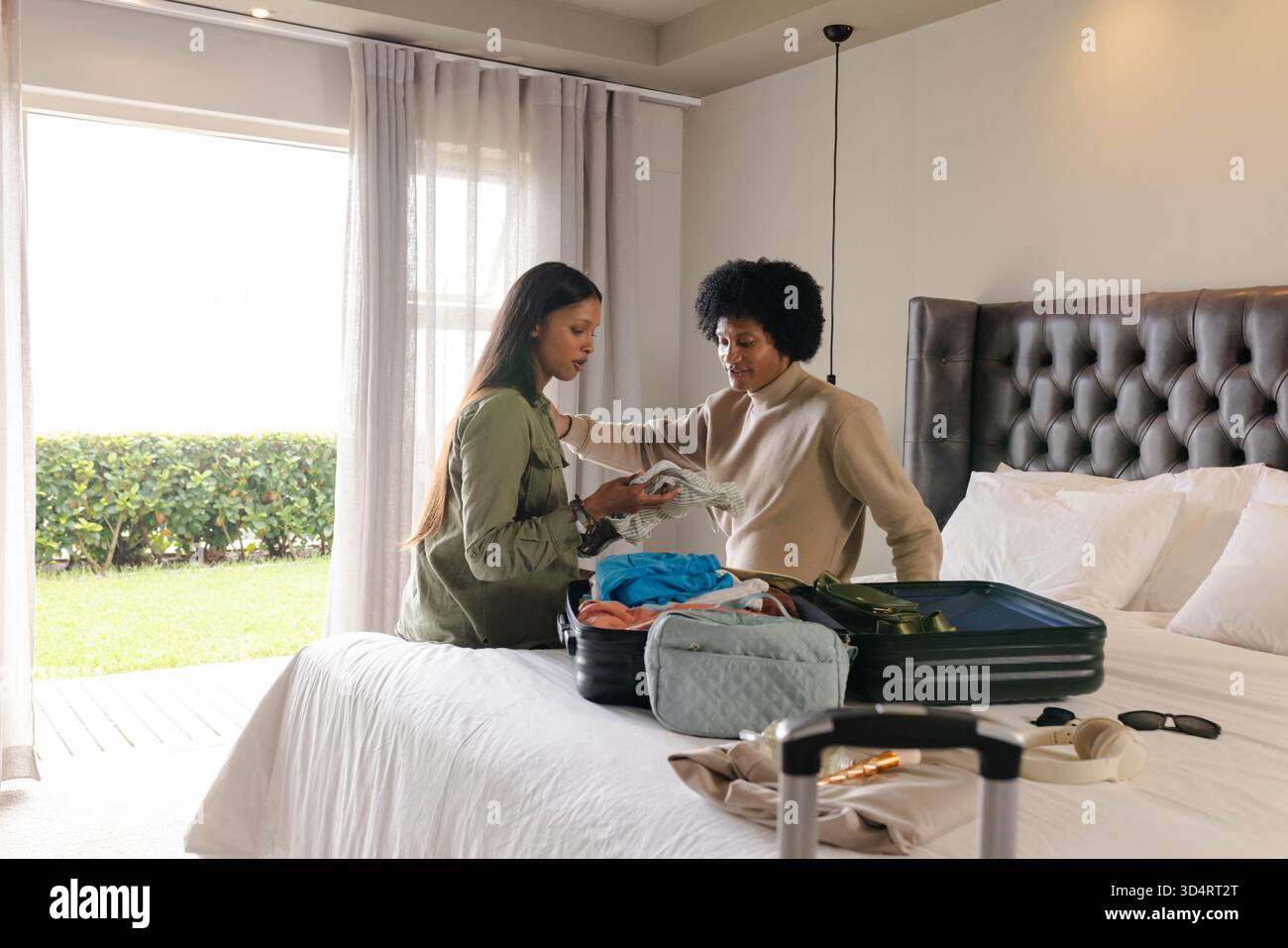 Verschiedene weibliche Freunde, die Kleidung auf einem großen Bett im Schlafzimmer packen, mit offenem Koffer und Reisetasche Stockfoto