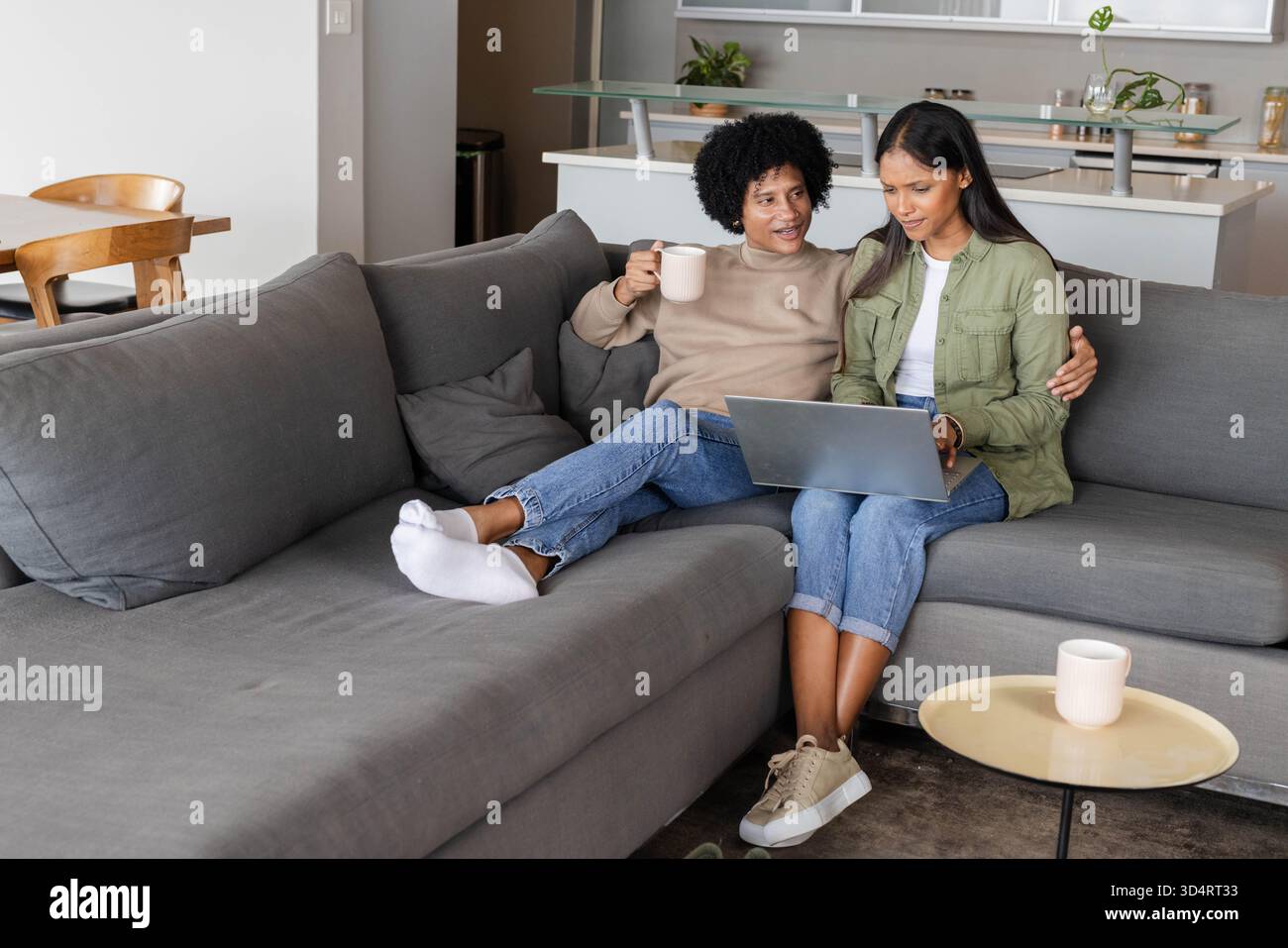 In einem offenen Wohnzimmer sitzen verschiedene Paare, die auf einem grauen Sofa mit Kaffeetassen in der Hand sind Stockfoto