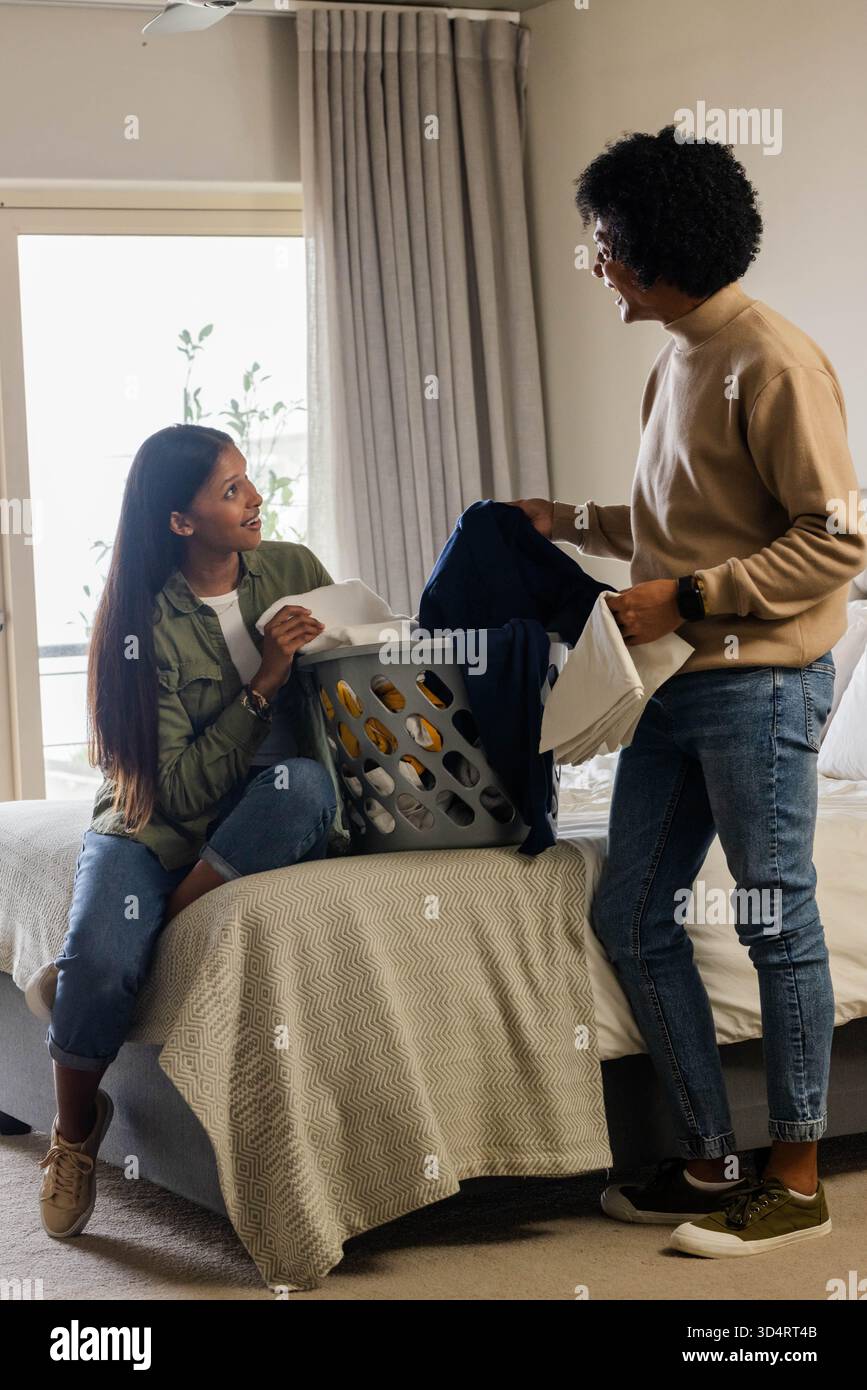 Diverse Mutter und Tochter sortieren Wäsche auf dem Bett im aufgeräumten Schlafzimmer, mit grauem Plastikkorb Stockfoto