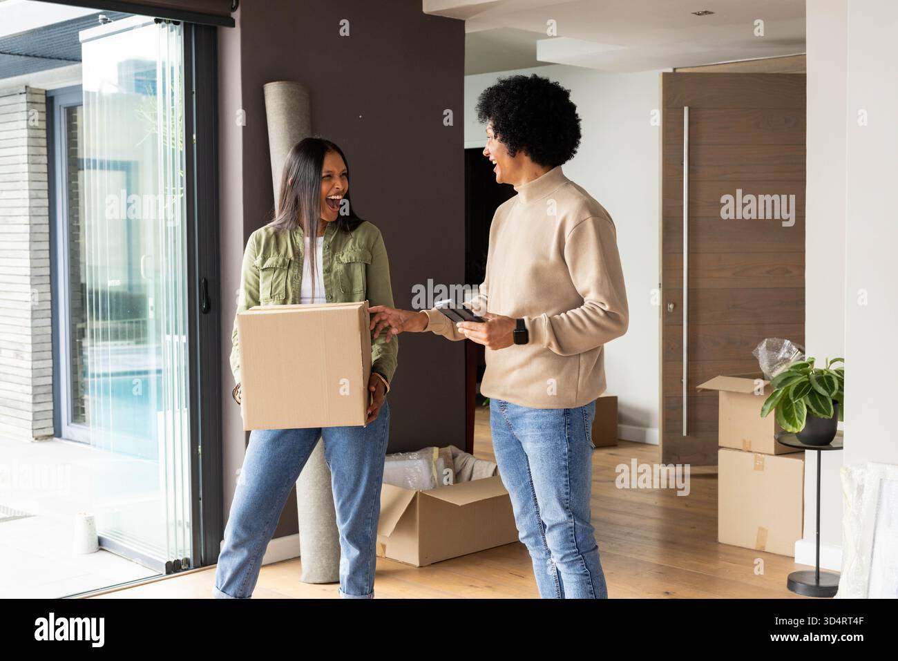 Mithilfe eines Handscanners, einer Zustellerin und einer indischen Frau, die Kartonschachteln im Wohnzimmer bewegt Stockfoto