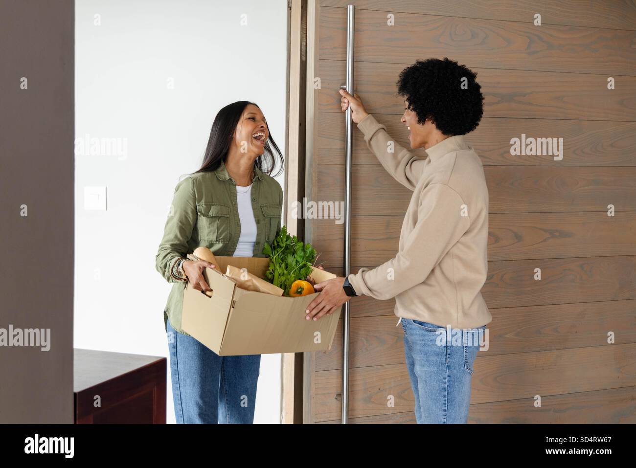 Verschiedene Nachbarn grüßen einander im Eingangsbereich, mit Holztür und Lebensmittelbox Stockfoto