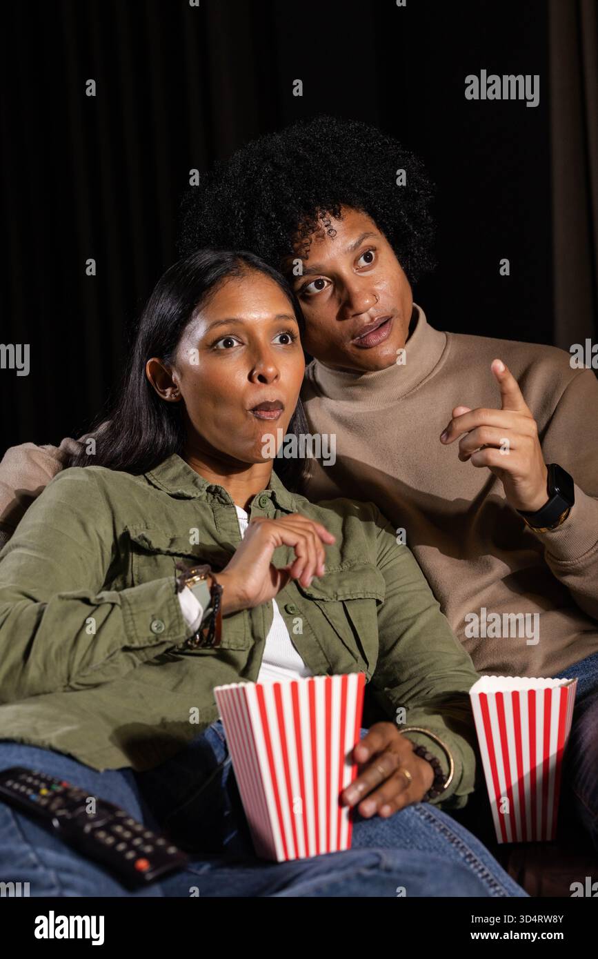 Beobachten Sie verschiedene Paare, die auf der Couch im Heimkino sitzen und Popcorn aus Eimern mit Fernbedienung essen Stockfoto