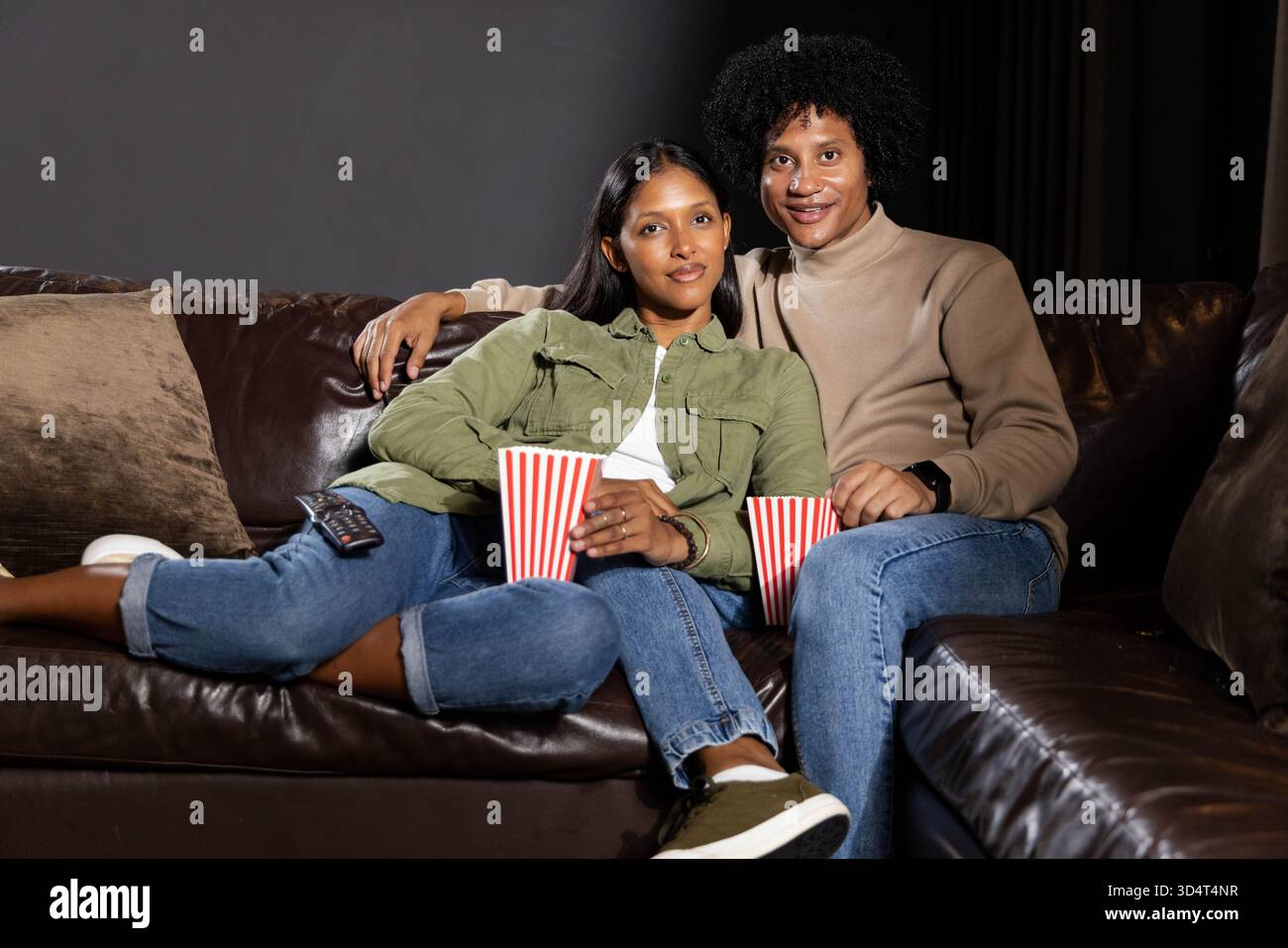 Mit gestreiften Popcorn-Eimern und TV-Fernbedienung, diverse Paare kuscheln sich auf der Couch im Wohnzimmer Stockfoto