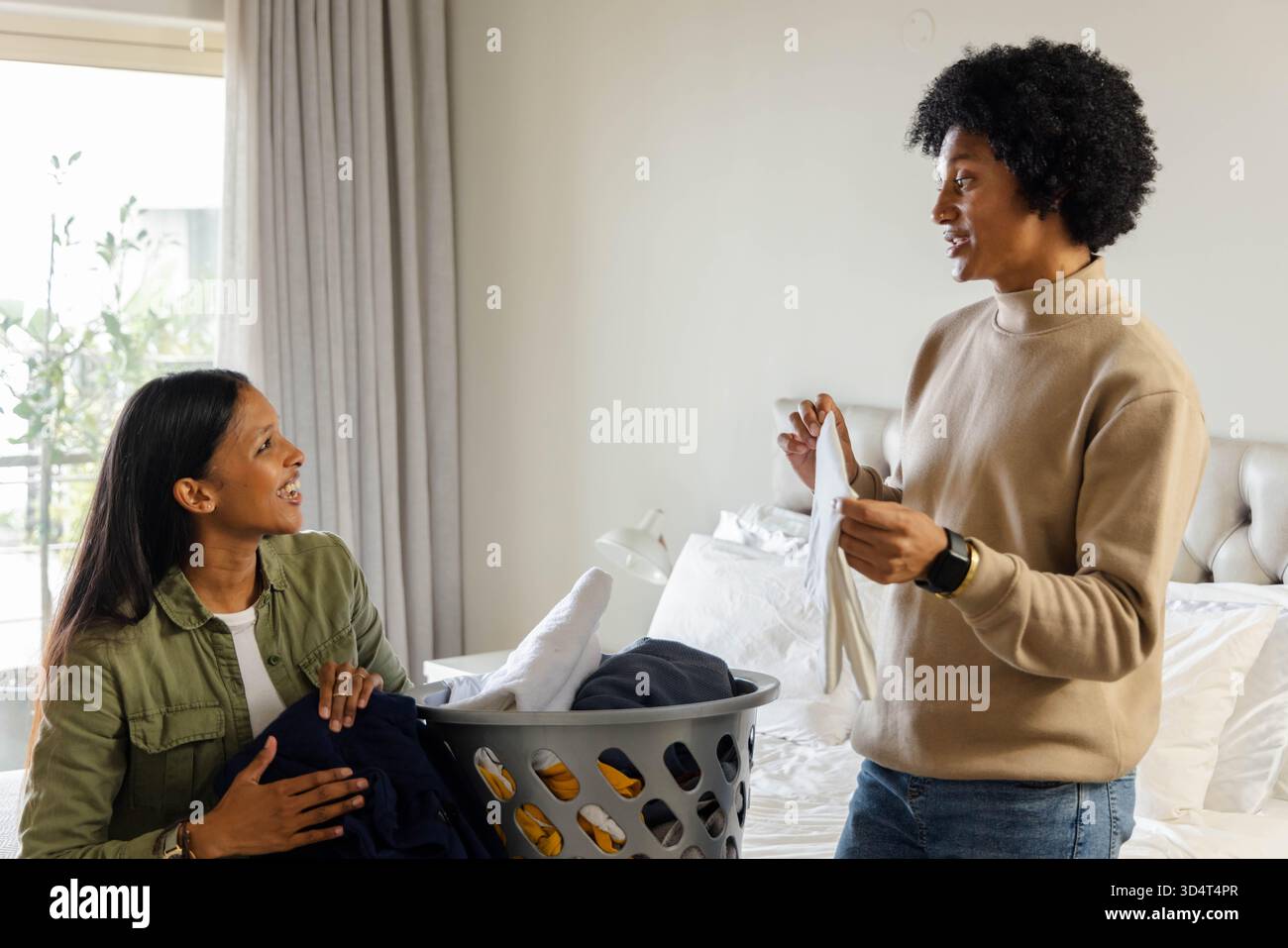 Diverse Sortiermöglichkeiten für Paare und Klappwäsche in hellem Schlafzimmer, mit Plastikwaschkorb und Bett Stockfoto