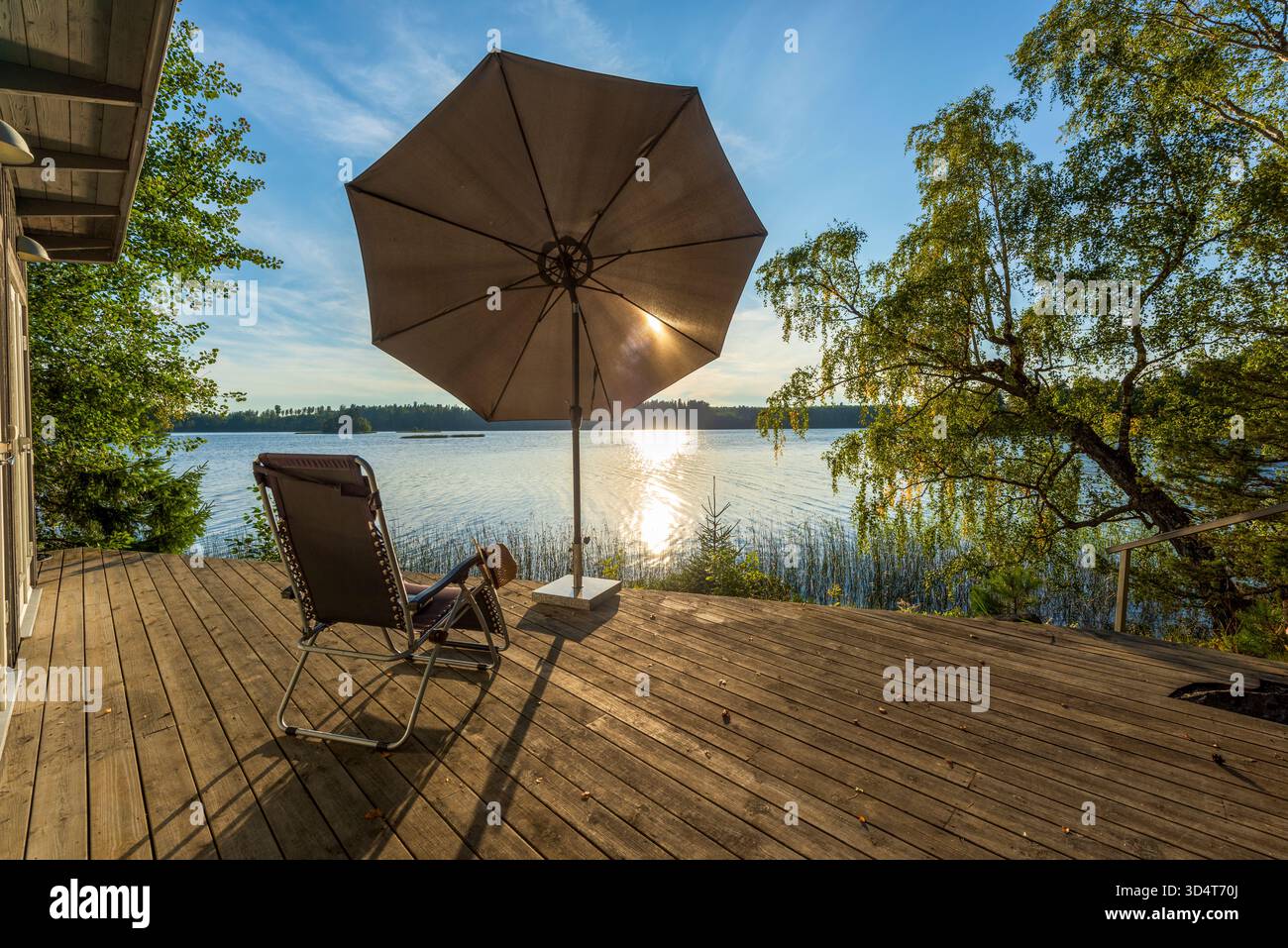 Ein Sonnenschirm und Liegestuhl auf einer Holzterrasse an einem Spätsommertag an einem See, Schweden Stockfoto