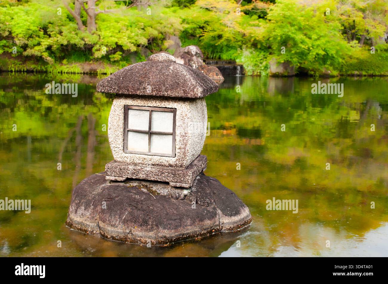 Traditionelle Steinlaterne neben einem reflektierenden Teich im japanischen Garten des Himeji. Stockfoto