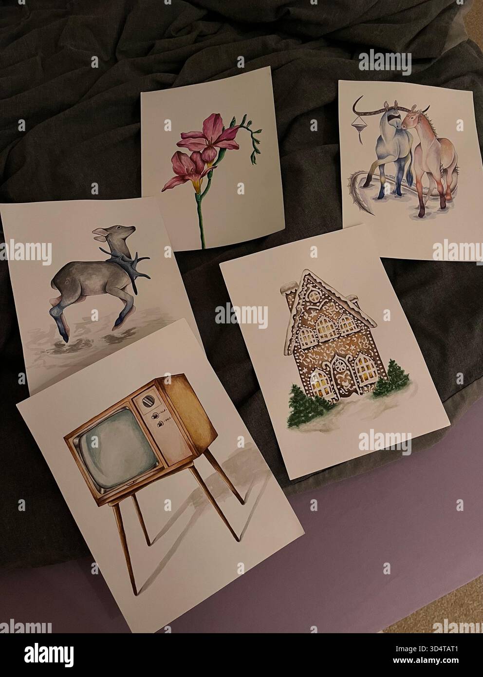 Eine flache Komposition aus mehreren Aquarellillustrationen, darunter Tiere, Blumen und ein Vintage-Fernseher, angeordnet auf einem dunklen Stoffhintergrund. Stockfoto