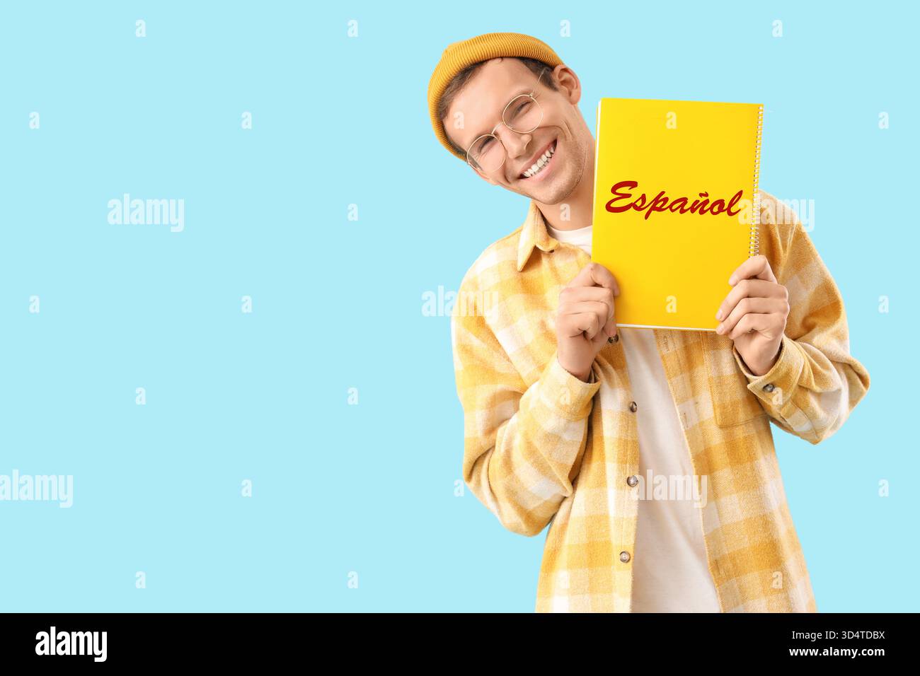 Junger Mann mit Buch auf blauem Hintergrund. Spanisch Lernen Stockfoto